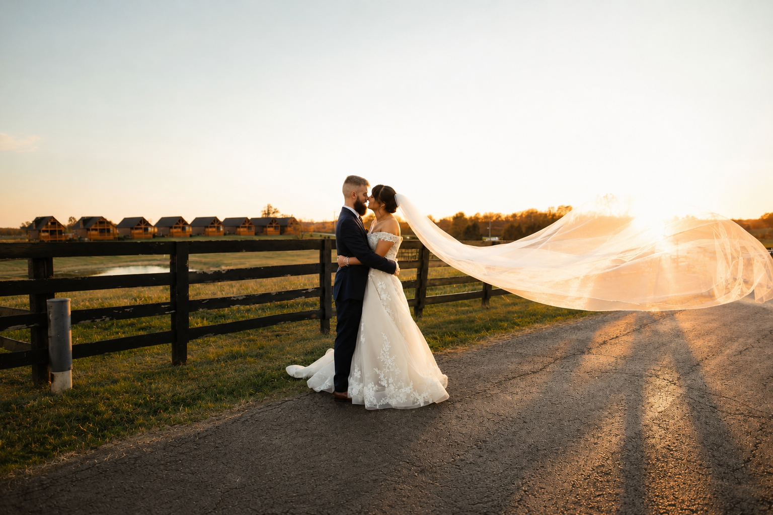 Bride and groom embracing by the fence with the cabins in the distance